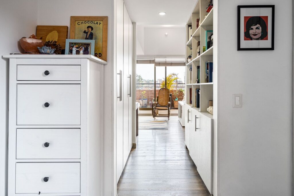 A modern hallway with storage leading to a bright room with a rocking chair in Bogotá, Colombia.