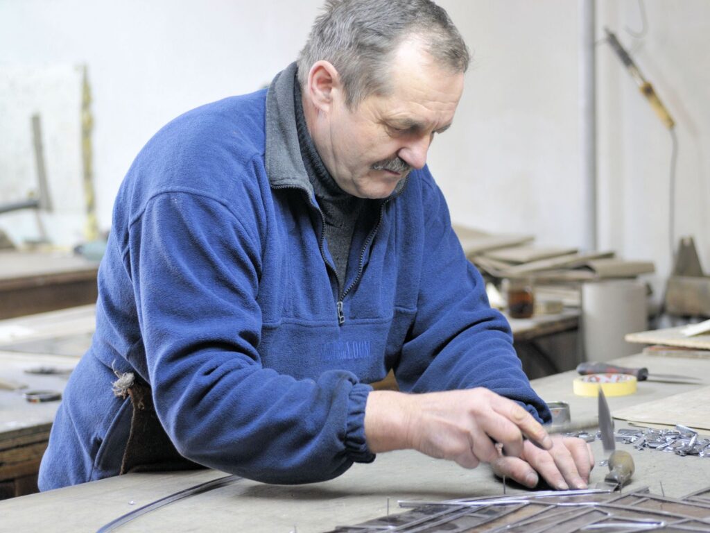 An elderly man focused on crafting metal pieces in a workshop setting.