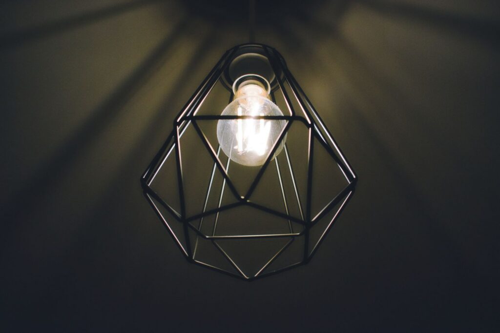 A modern geometric pendant light bulb in a dark room, casting warm, soothing illumination.