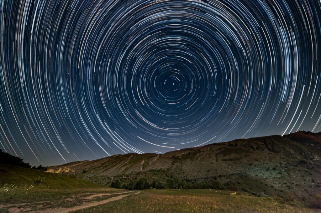 Captivating star trails forming circles above a serene mountain scene, captured with long exposure.