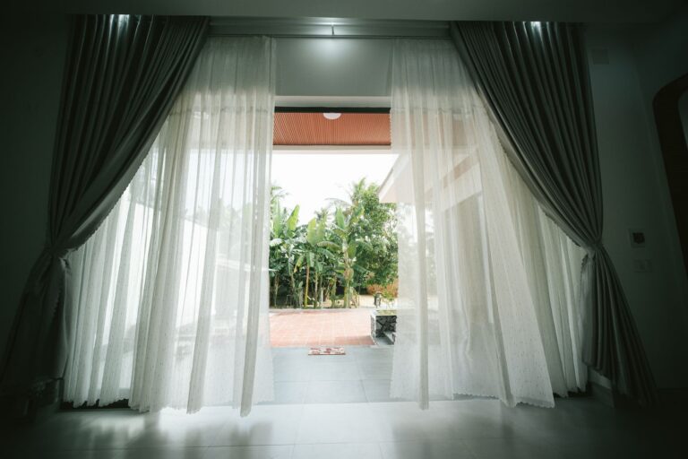 View of open terrace through white curtains, revealing a lush garden.