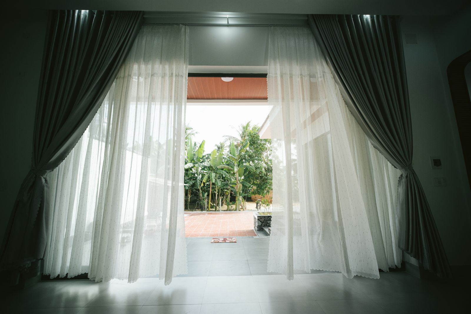 View of open terrace through white curtains, revealing a lush garden.