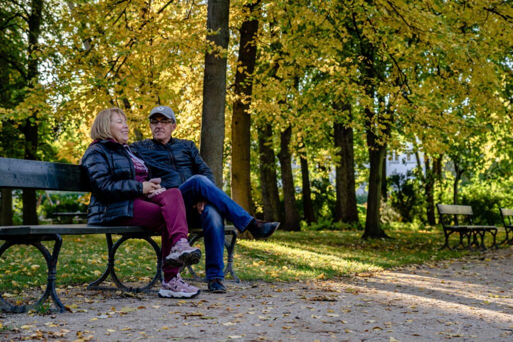 Happy senior couple sitting on a park bench surrounded by autumn foliage.