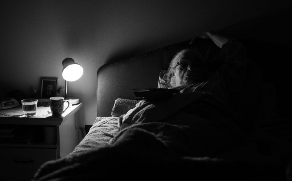 A senior woman lying in bed under a lamp, conveying solitude and tranquility.