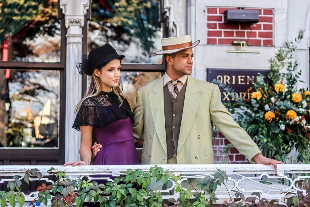 Elegantly dressed couple posing on a vintage-style balcony, exuding retro charm.