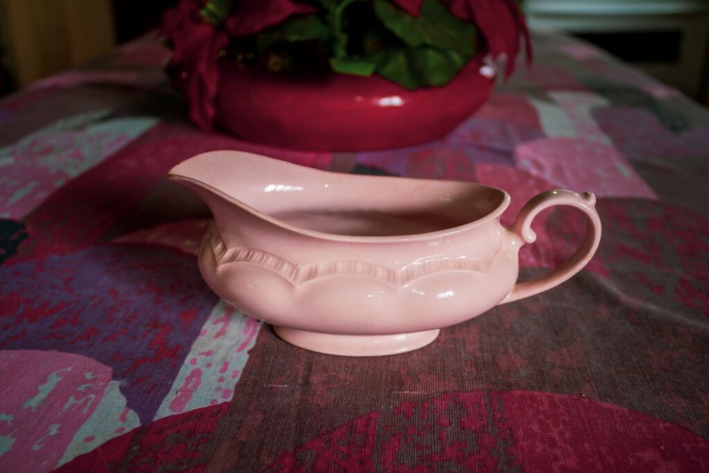 Retro pink porcelain gravy boat on a vibrant tablecloth indoors.