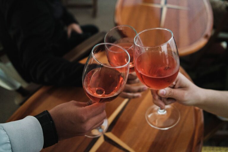 Three friends toasting with rosé wine glasses over a wooden table indoors.