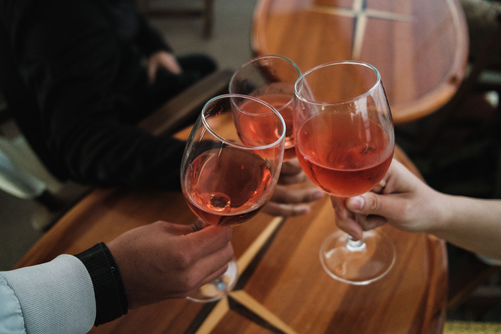 Three friends toasting with rosé wine glasses over a wooden table indoors.