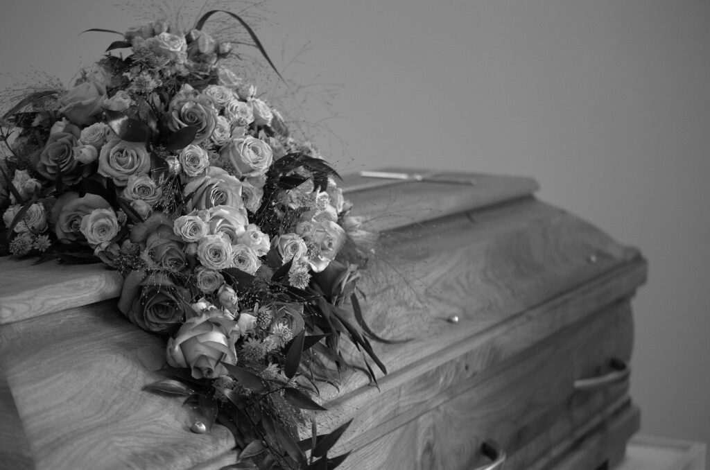 A black and white image featuring a wooden casket adorned with a vibrant floral bouquet, symbolizing respect and memory.