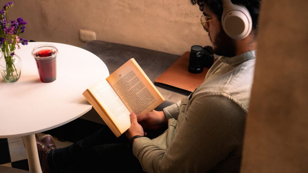 A man sitting in a café enjoys a book while listening to music, creating a serene atmosphere.