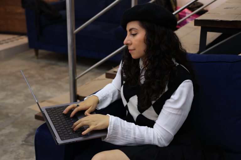 Young woman in a beret using a laptop indoors. Style meets technology.