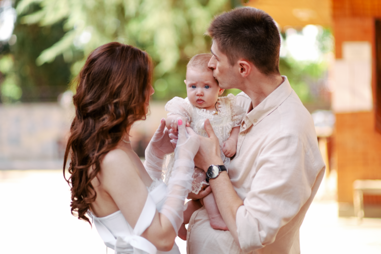 Happy young parents lovingly embracing their baby in a sunny outdoor setting.