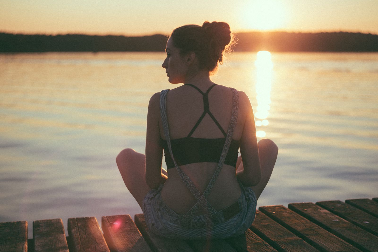 A calm moment of relaxation as a woman sits on a dock, gazing at the sunset over a serene water body.