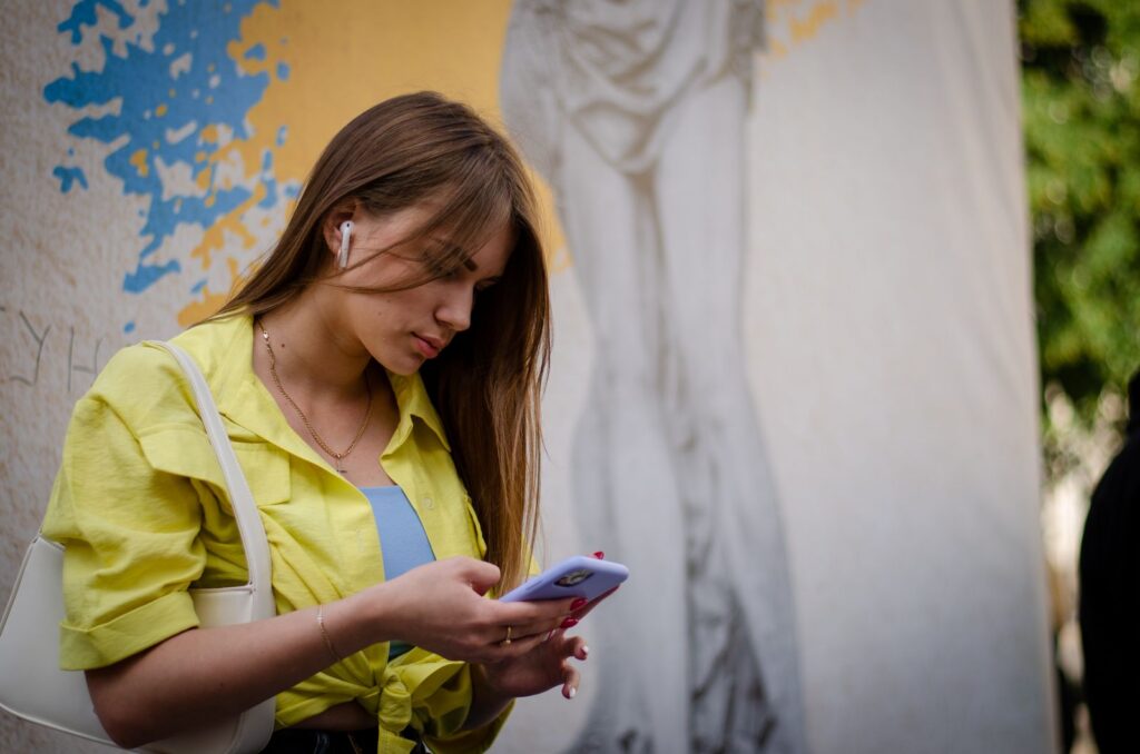 Young woman with earphones, smartphone, and graffiti background on a city street.