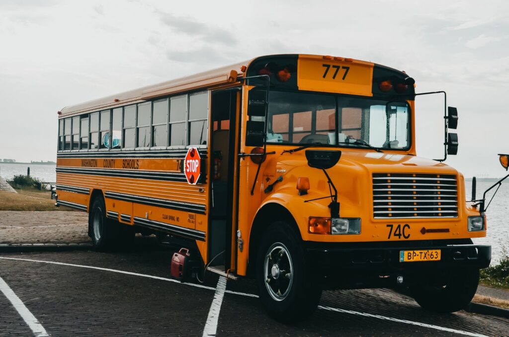 Classic American yellow school bus parked by a serene lakeside in an urban setting.
