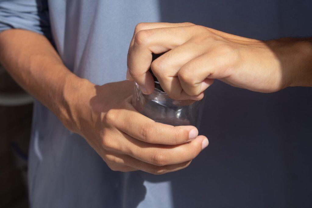 Close-up view of hands opening a jar outdoors, emphasizing grip and strength.