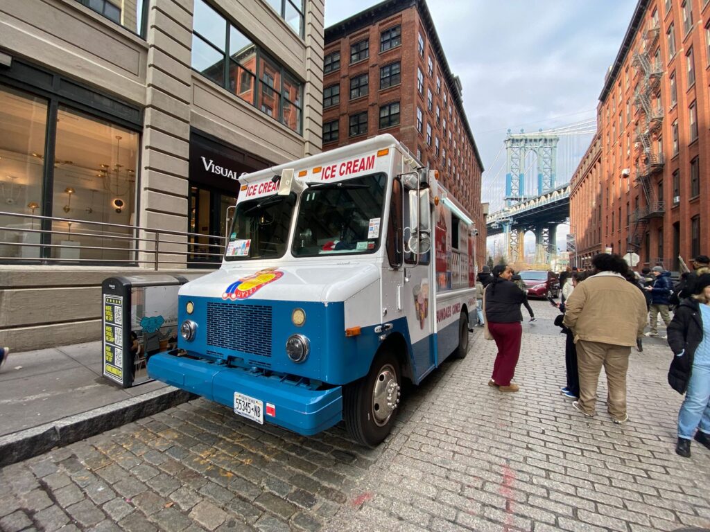 Ice cream truck parked on a bustling street near the Manhattan Bridge in New York City.