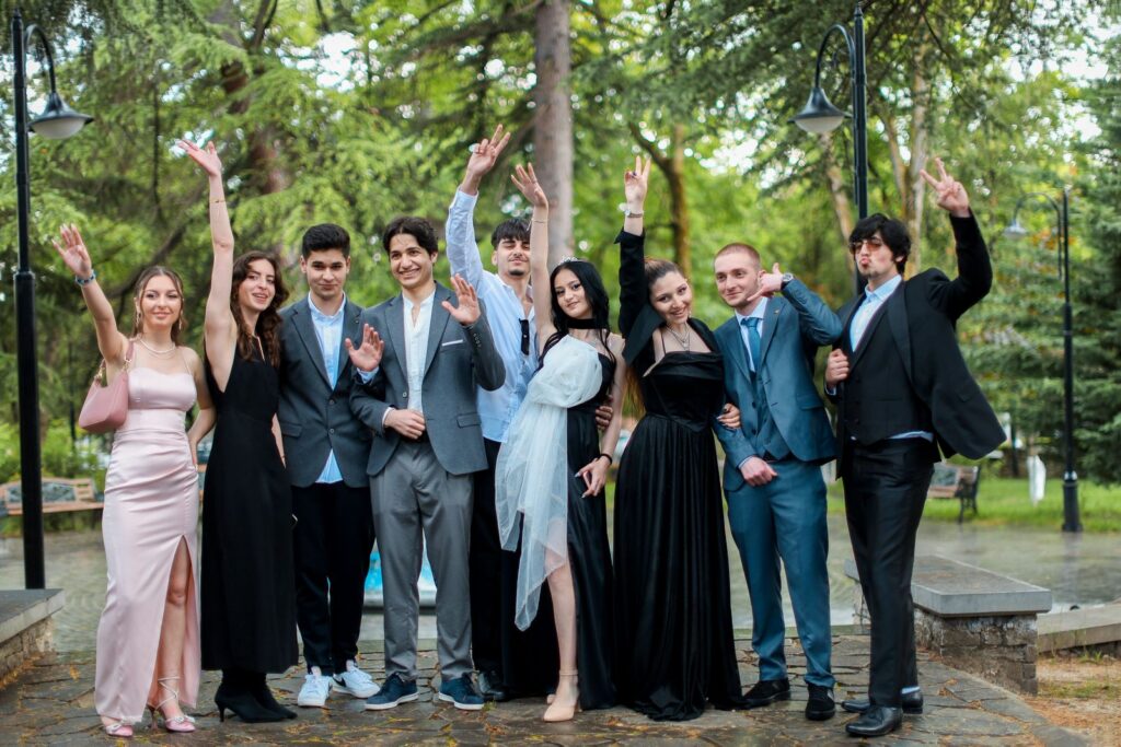 A group of young adults in formal attire celebrating outdoors with cheerful expressions.
