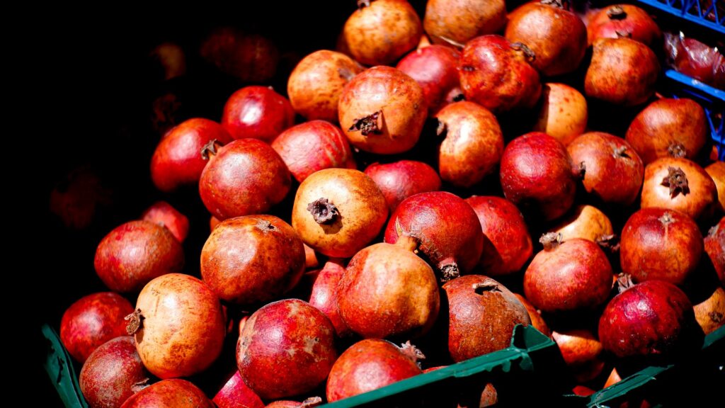 An inviting arrangement of fresh pomegranates in a market crate glows under natural light, showcasing their rich color.