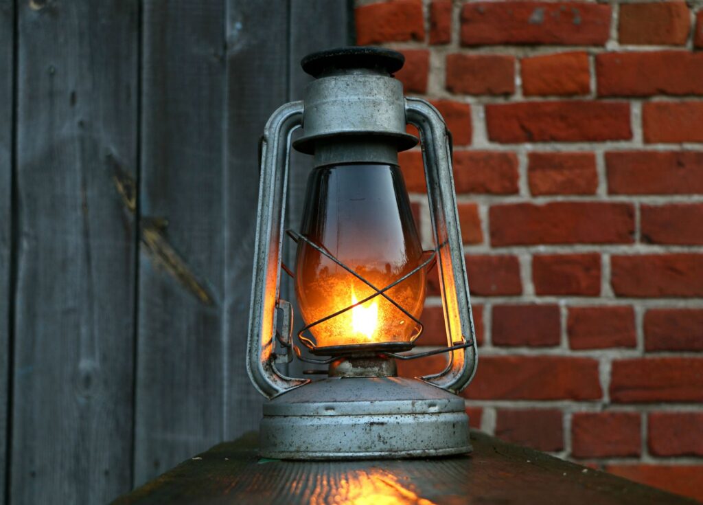 Close-up of an antique oil lantern casting a warm glow against a rustic red brick wall.