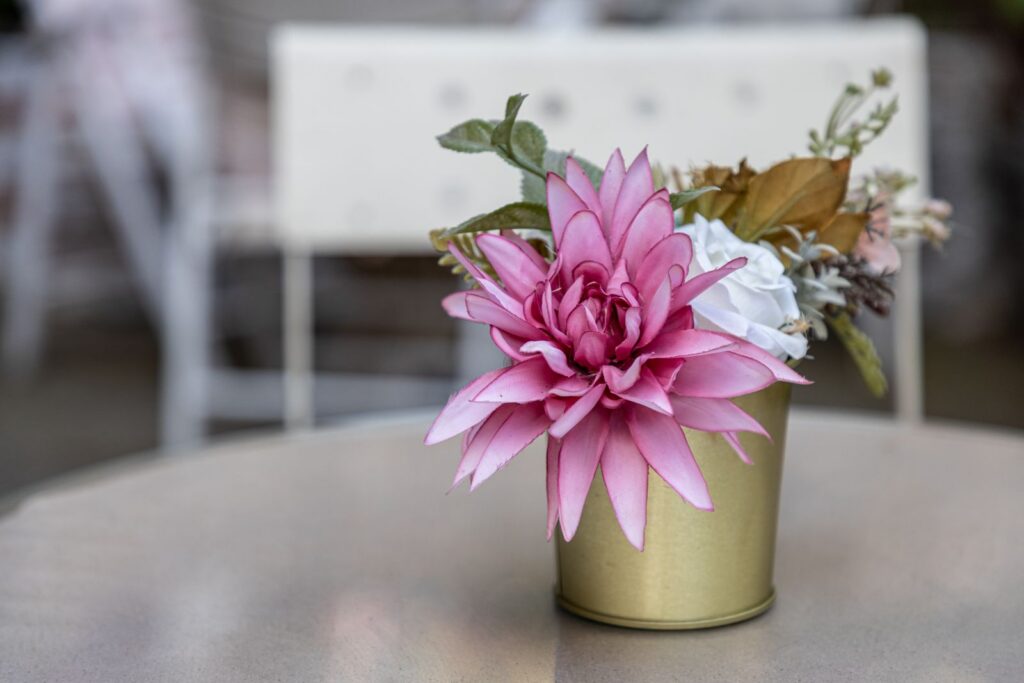 Bright pink artificial dahlia in a gold pot outdoors on a table, perfect for decoration.