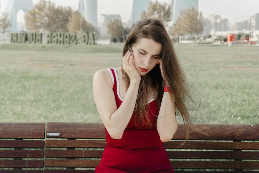 Woman in red dress sitting on a bench outdoors.
