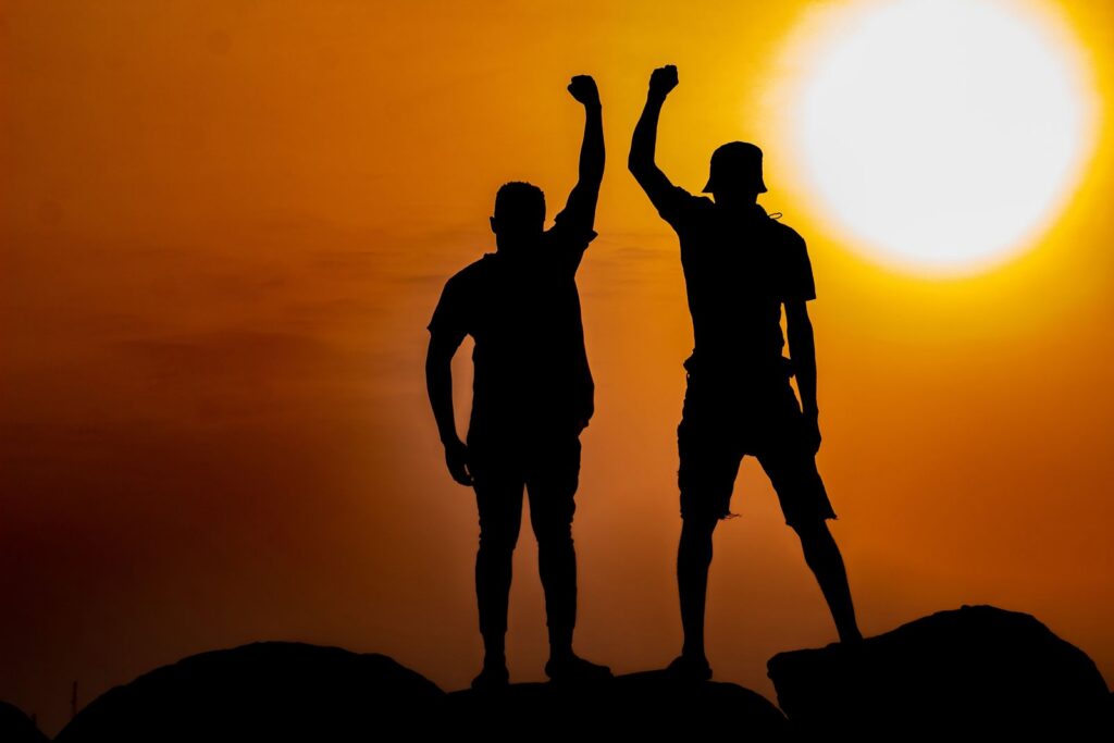 Two silhouetted figures raising fists triumphantly against a vibrant sunset in Ghana.