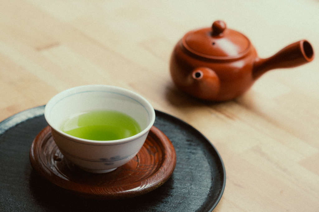 A cup of vibrant green tea and a clay teapot on wooden surface, capturing a calming essence.