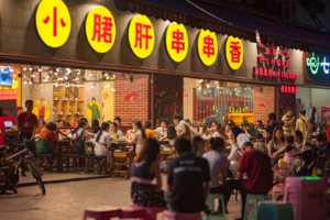 Busy evening scene at an Asian street food restaurant with a crowd enjoying dining outdoors.