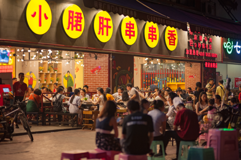Busy evening scene at an Asian street food restaurant with a crowd enjoying dining outdoors.