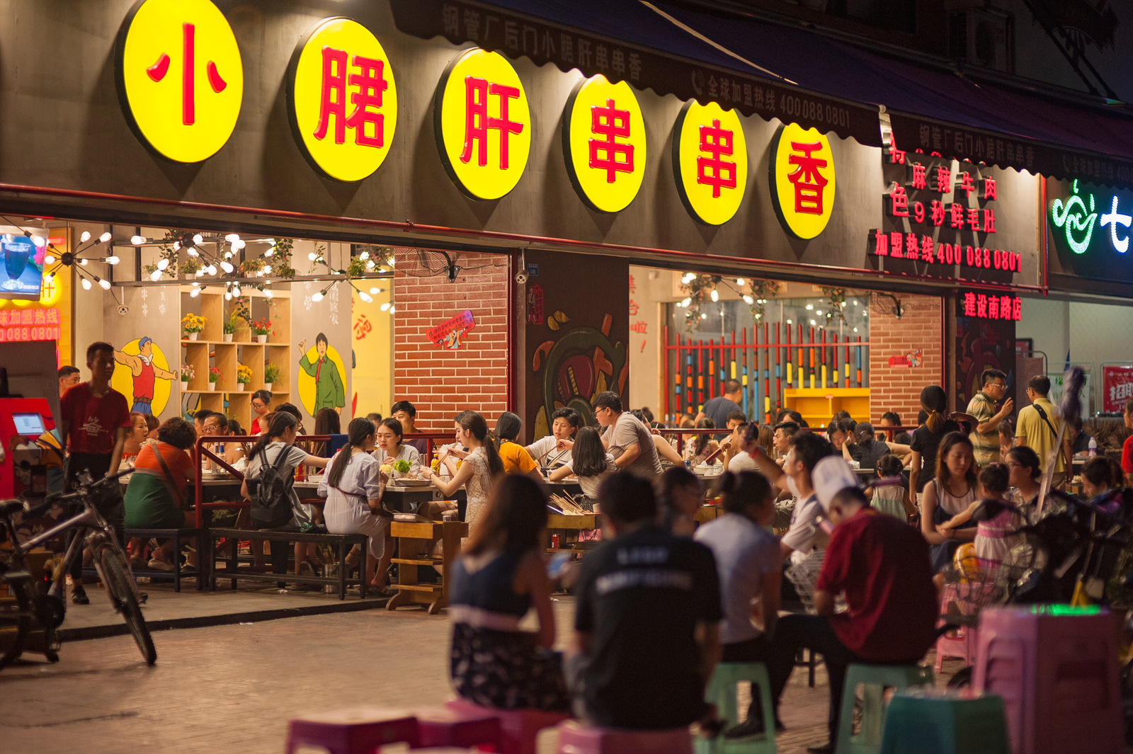 Busy evening scene at an Asian street food restaurant with a crowd enjoying dining outdoors.