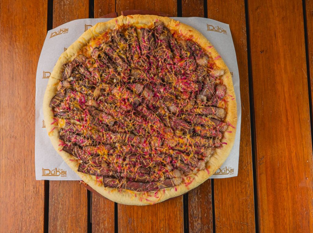Appetizing meat-loaded pizza with shredded cheese, served on a wooden table for a perfect meal.