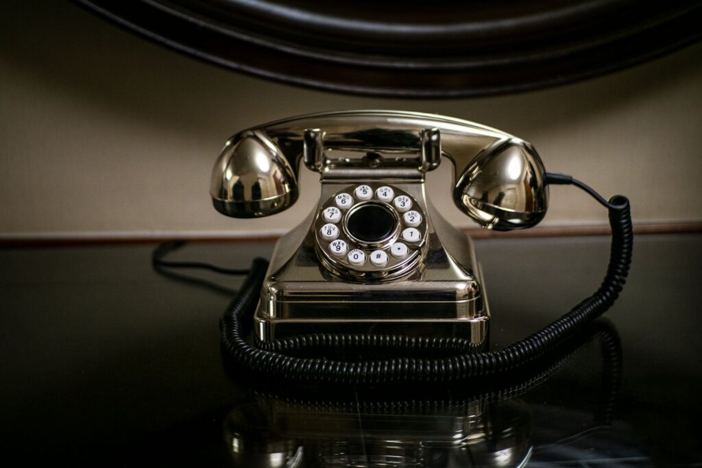 A shiny vintage dial telephone with a coiled cord on a dark reflective surface.