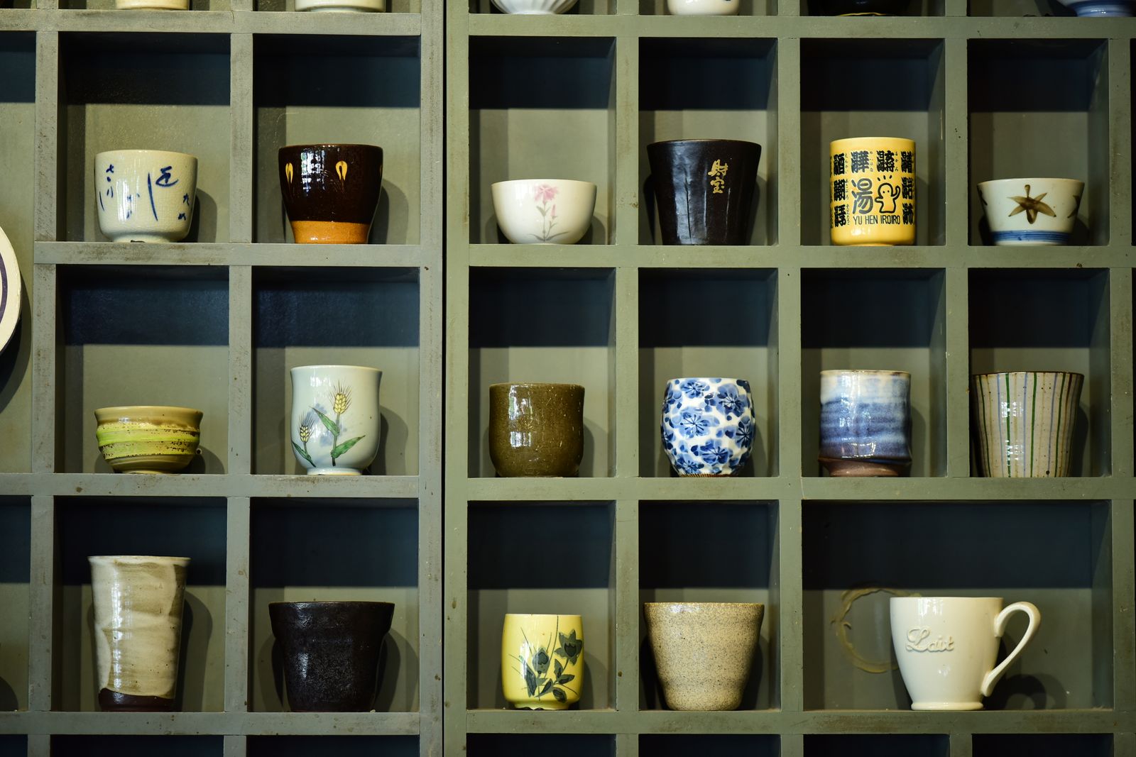 Collection of colorful ceramic mugs showcased on a wooden shelf in grid design.