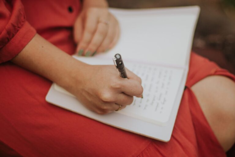 Close-up of a woman writing in a journal outdoors, capturing a serene moment in nature.
