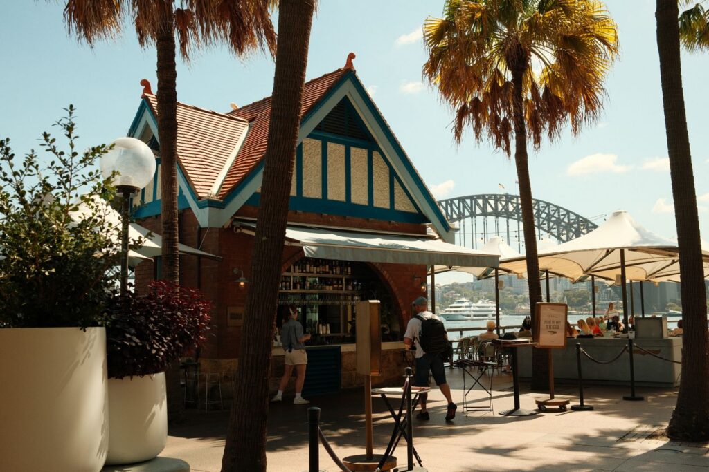 Outdoor cafe near Sydney Harbour Bridge with palm trees and a relaxed atmosphere.