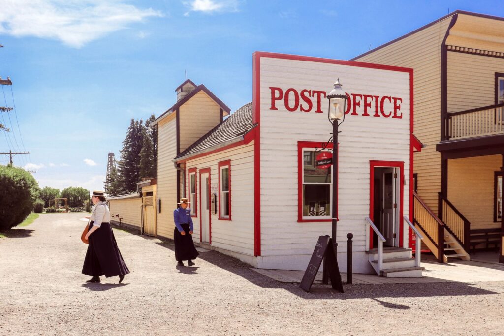 Vintage-style photo of a historic post office at Heritage Park in Calgary with people in period attire.