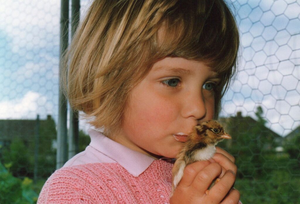 Little girl gently holds a chick outside, showcasing innocence and nature connection.