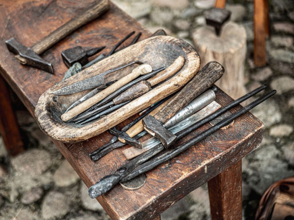 A collection of vintage blacksmith tools displayed on a wooden table outdoors.