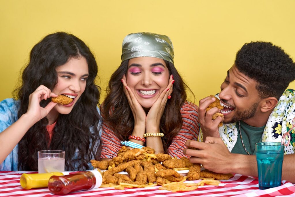 Three friends indulge in a joyful fried chicken meal at a colorful table setting.