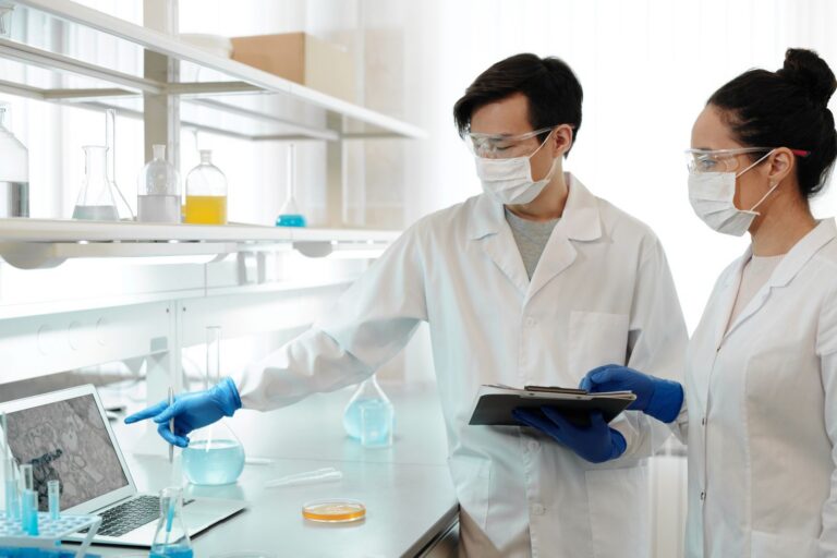 Two scientists in lab coats examining data on a computer in a research laboratory.