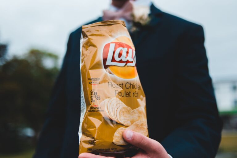 Anonymous male showing sack with chips while resting in countryside on summer day
