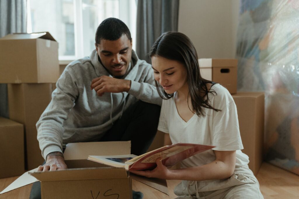 A couple sitting together, unpacking boxes and reminiscing with a photo album in their new home.