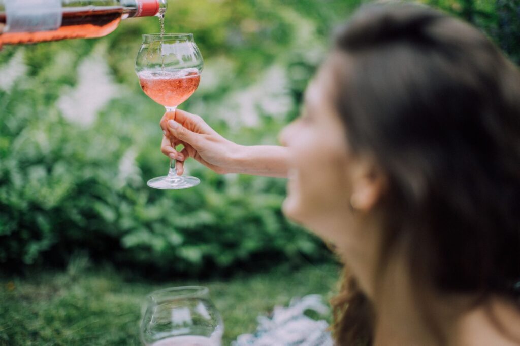 A woman elegantly pours rosé wine into a glass during a sunny outdoor picnic, capturing a relaxed summer vibe.
