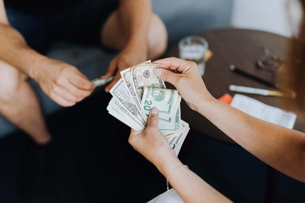 Close-up of people handling and counting US dollar bills indoors.