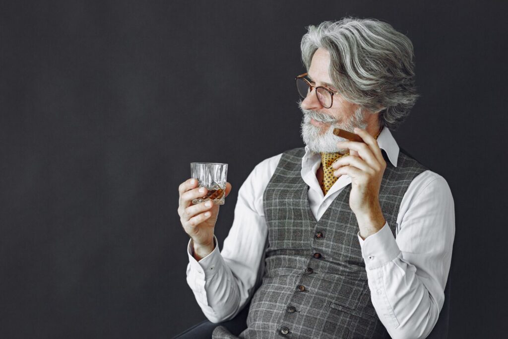 Distinguished elderly man enjoying a cigar and whiskey with a contemplative expression.