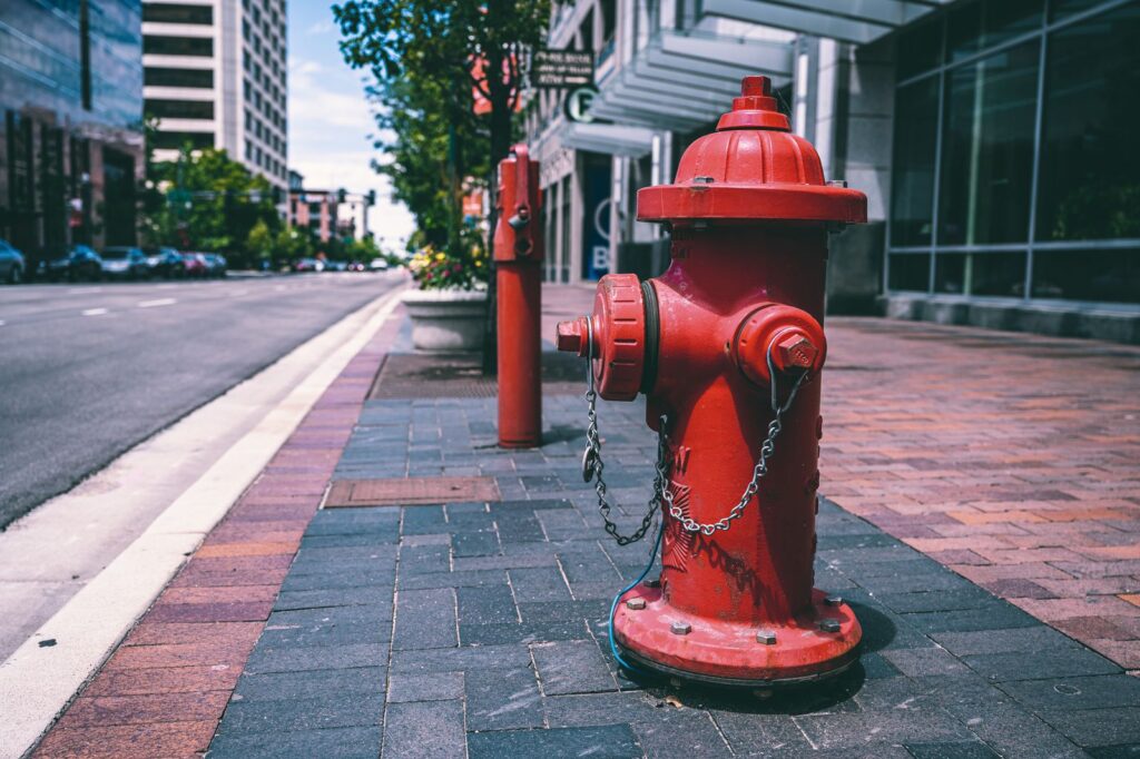 Red fire hydrant with chains located on empty street near road and building on sunny day