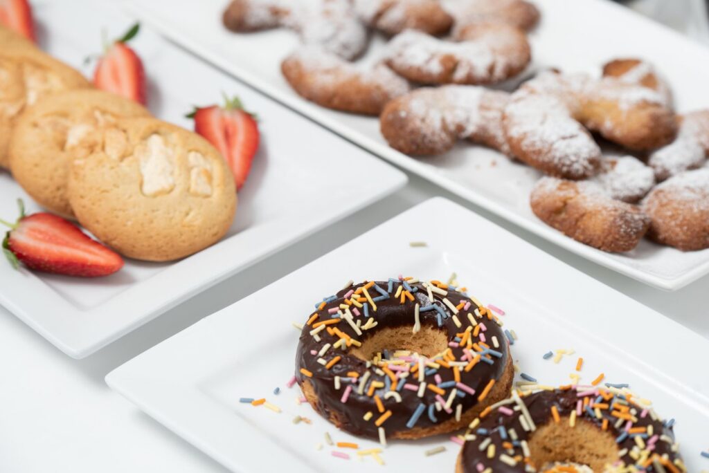 A tempting display of cookies, doughnuts, and pastries on white plates with strawberries.