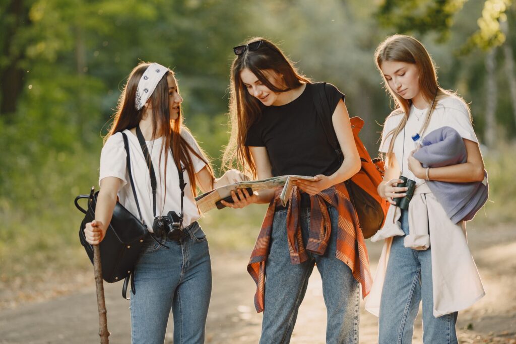 Three young women hiking in a forest while reading a map, enjoying a sunny day.