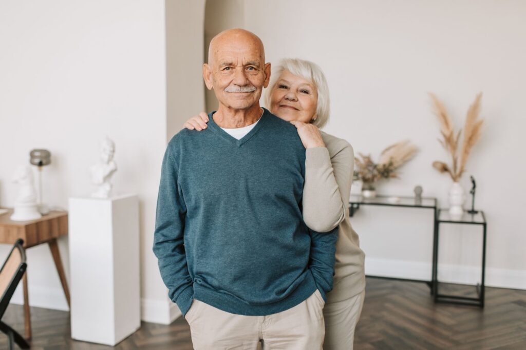 A smiling elderly couple embracing happily indoors, showcasing love and togetherness.